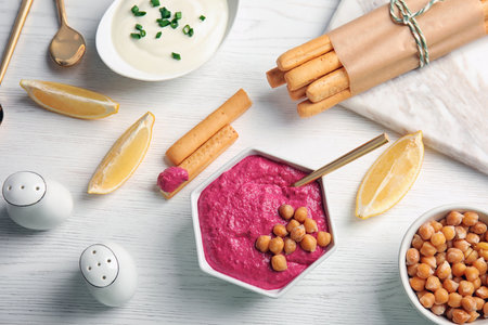 Flat lay composition with bowl of tasty beet hummus, bread sticks and chickpea on light table
