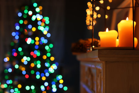 Burning candles on fireplace and Christmas tree with fairy lights at night. Stylish room interiorの写真素材
