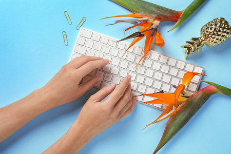 Woman using computer keyboard on table decorated with tropical flowers, top view. creative design ideasの写真素材