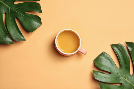 Flat lay composition with cup of tea and tropical leaves on color backgroundの写真素材