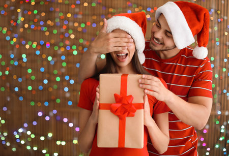 Young couple in Santa hats with Christmas gift on blurred lights backgroundの写真素材