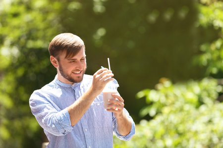 Young man with cup of delicious milk shake outdoorsの写真素材