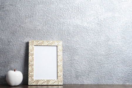 Blank frame and decorative apple figure on table near color wall. Mock up design