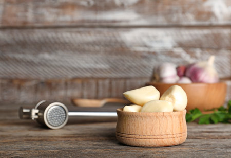 Garlic press and bowl with cloves on tableの写真素材