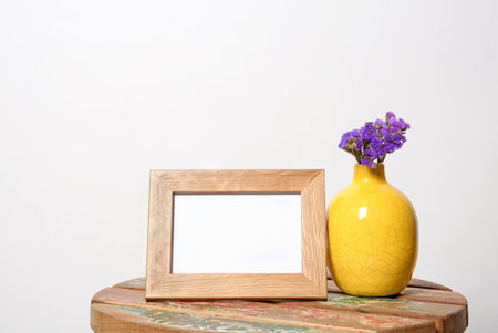 Blank frame and vase with flowers on table against white background. Mock up designの写真素材