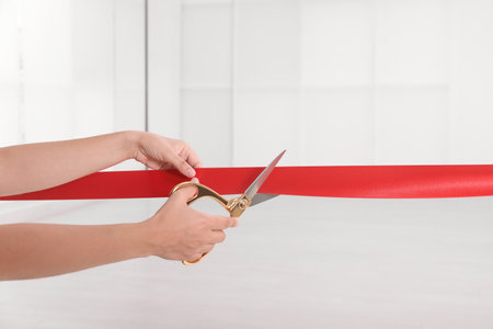 Woman cutting red ribbon on blurred background. Festive ceremonyの写真素材