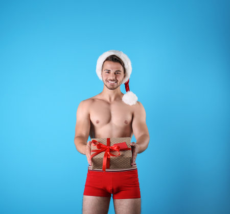 Shirtless sexy young Santa Claus with gift on color backgroundの写真素材