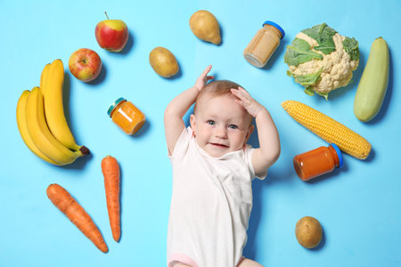 Cute little child with ingredients and purees in jars on color background, top view. baby foodの写真素材