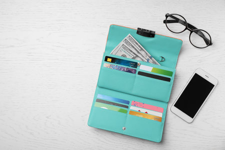 Smartphone, glasses and stylish wallet with cash and credit cards on light background, top view