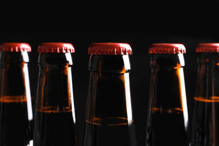 Bottles of tasty cold beer on black background, closeup