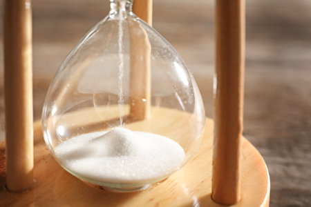 Hourglass with flowing sand on table, closeup. time management