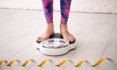 Woman measuring her weight using scales on floorの写真素材