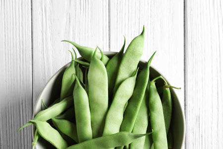 Bowl with fresh green beans on wooden table