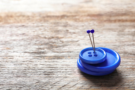 Blue buttons with pins on wooden background. tailoring equipmentの写真素材