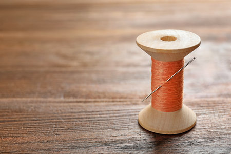 Spool of thread with needle on wooden background. tailoring equipmentの写真素材