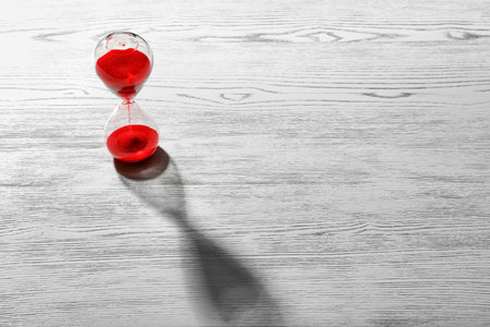 Hourglass with flowing red sand on wooden background. time managementの写真素材