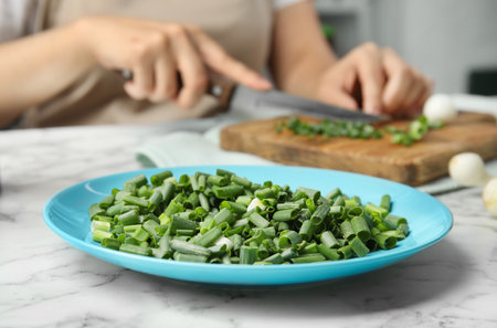 Plate with chopped green onion and blurred woman on backgroundの写真素材