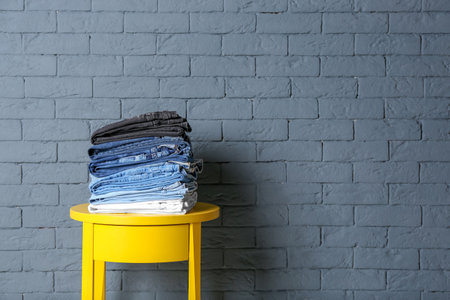 Stack of different jeans on table against brick wall
