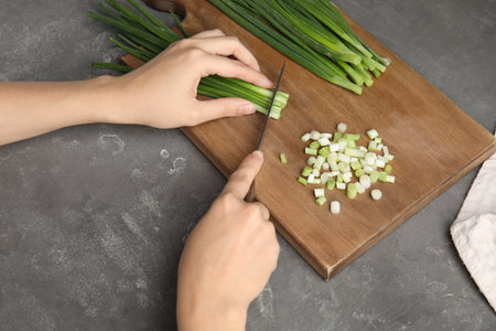 Woman cutting fresh green onion on wooden boardの写真素材