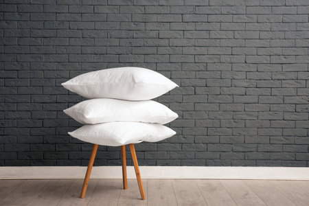 Pile of soft bed pillows on chair near brick wall with space for textの写真素材