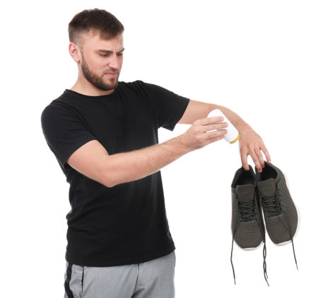 Young man putting powder freshener into shoes on white background