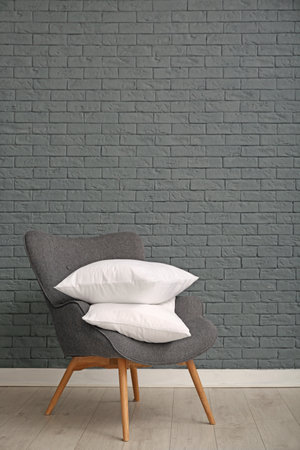 Pile of soft bed pillows on armchair near brick wall with space for textの写真素材