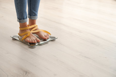 Woman with tape measuring her weight using scales on wooden floor. healthy diet