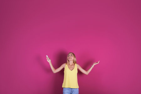Young woman operating air conditioner with remote control on color background