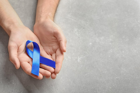 Man holding blue ribbon on gray background. cancer awarenessの写真素材