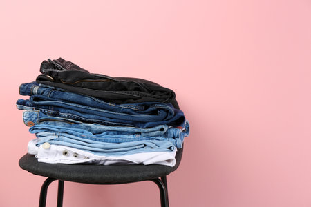 Stack of different jeans on stool against color background