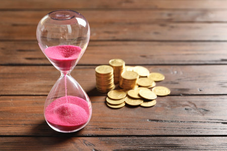 Hourglass and coins on table. time management