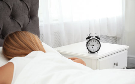 Analog alarm clock and sleepy woman in the bedroom. Time of dayの写真素材