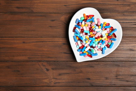 Heart shaped plate with different pills on wooden background. cardiology conceptの写真素材