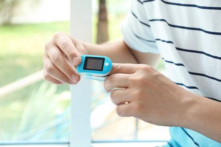 Young man checking pulse with blood pressure monitor on finger against blurred background, closeupの写真素材
