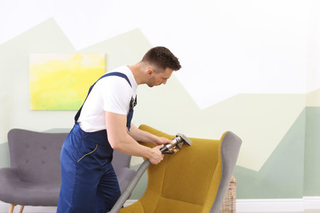 Male worker removing dirt from armchair with professional vacuum cleaner indoorsの写真素材