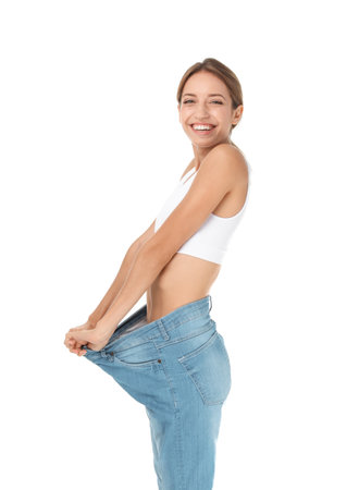 Young slim woman in old big jeans showing her diet results on white backgroundの写真素材