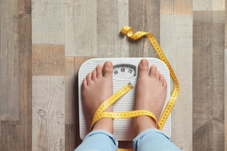 Woman with tied legs measuring her weight using scales on floor. healthy dietの写真素材