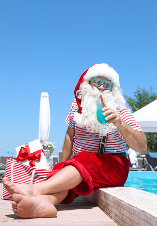 Authentic Santa Claus with cocktail and gift in bag near pool at resortの写真素材