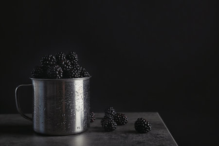 Mug with fresh blackberry on gray table against dark background. Space for textの写真素材