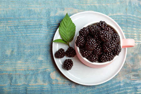 Mug of fresh blackberry on wooden background, top view