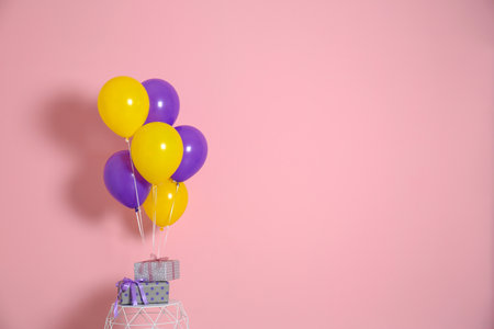 Bunch of bright balloons and gifts on table against color wall. Space for textの写真素材