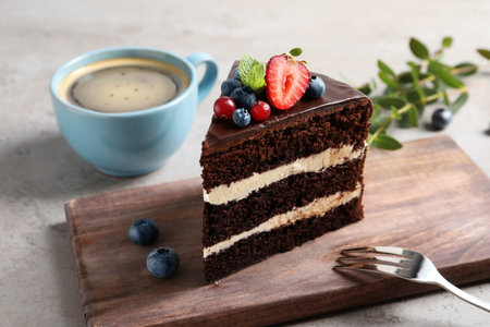 Wooden board with chocolate sponge berry cake and cup of coffee on gray backgroundの写真素材