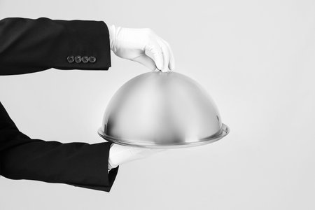 Waiter holding metal tray with lid on light backgroundの写真素材