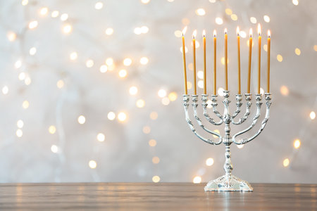 Hanukkah menorah with candles on table against blurred lightsの写真素材