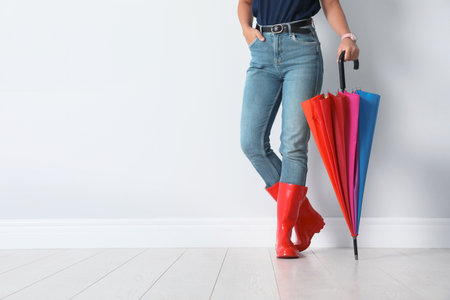 Woman in gumboots holding bright umbrella near white wall with space for designの写真素材