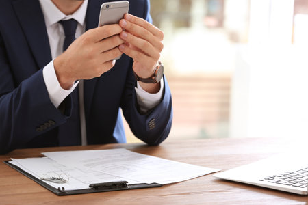 Real estate agent with smartphone at table in office, closeupの写真素材