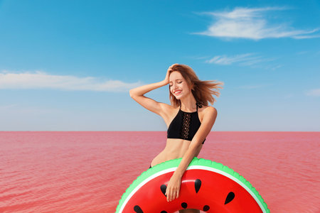 Beautiful woman with inflatable ring posing near pink lake on sunny dayの写真素材