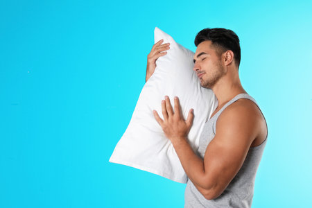 Young man with soft pillow on color backgroundの写真素材