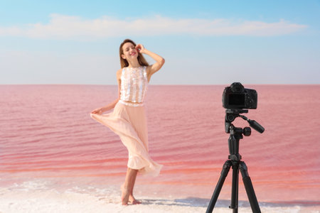 Young woman posing in front of professional camera near pink lake on sunny dayの写真素材