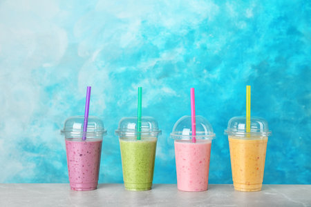Plastic cups with smoothies on table against color backgroundの写真素材